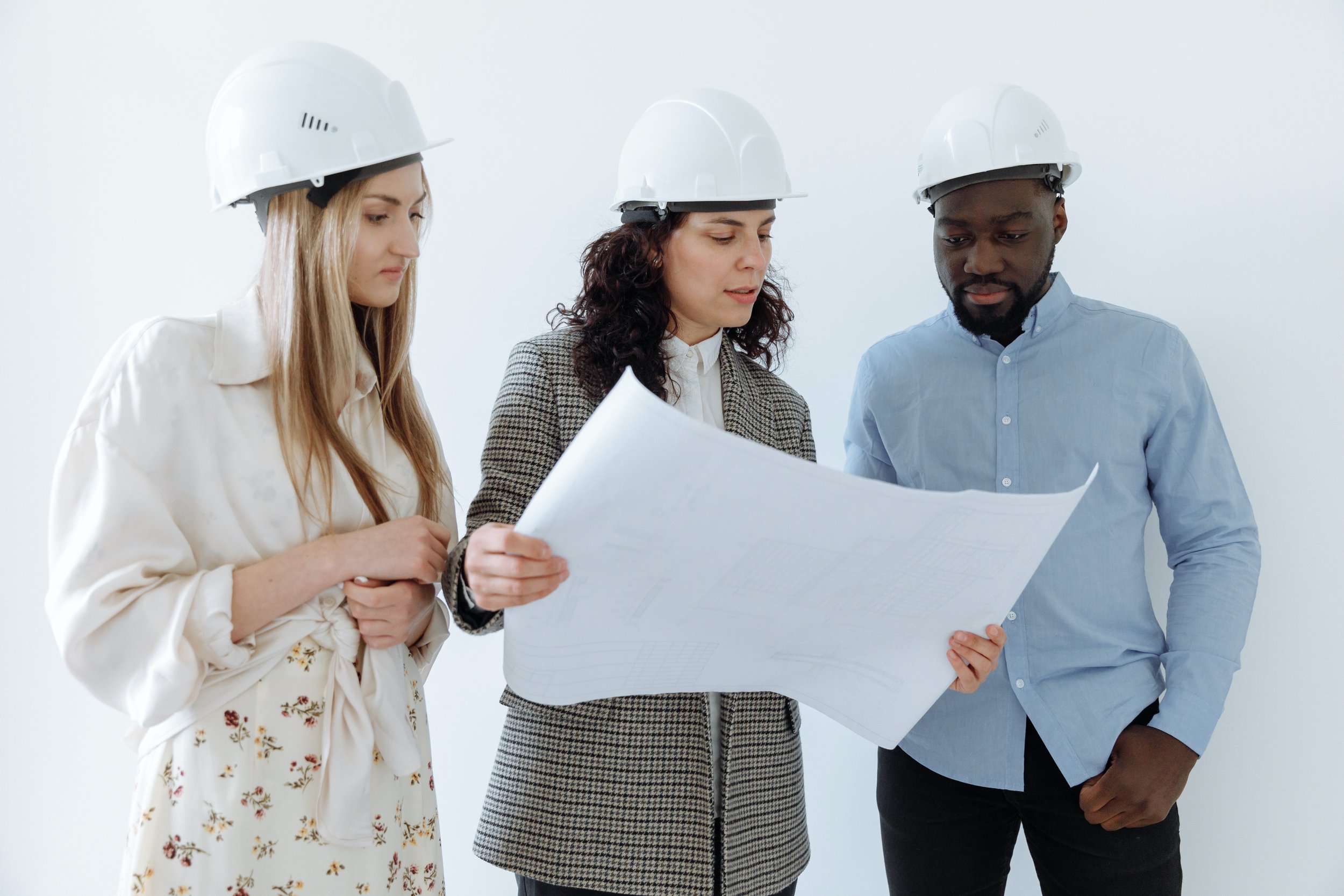 3 people in hard hats looking at a house remodeling plan