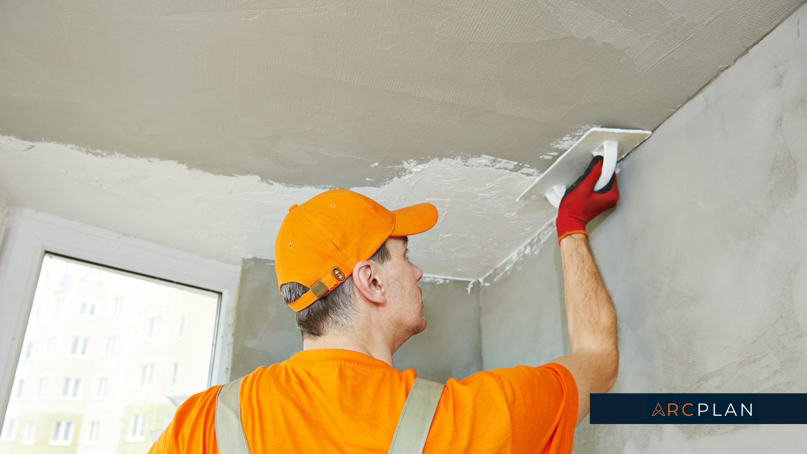 A man in an orange shirt and ha putting caulk on the ceiling.