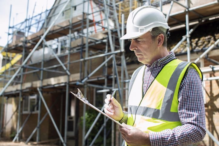 A builder using a writing tablet on a house construction project site.