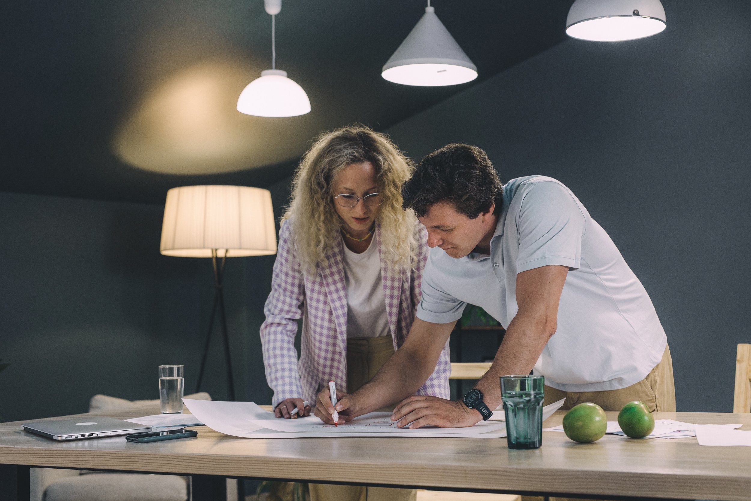 A man and a woman drawing with red marker on a plan on a table.